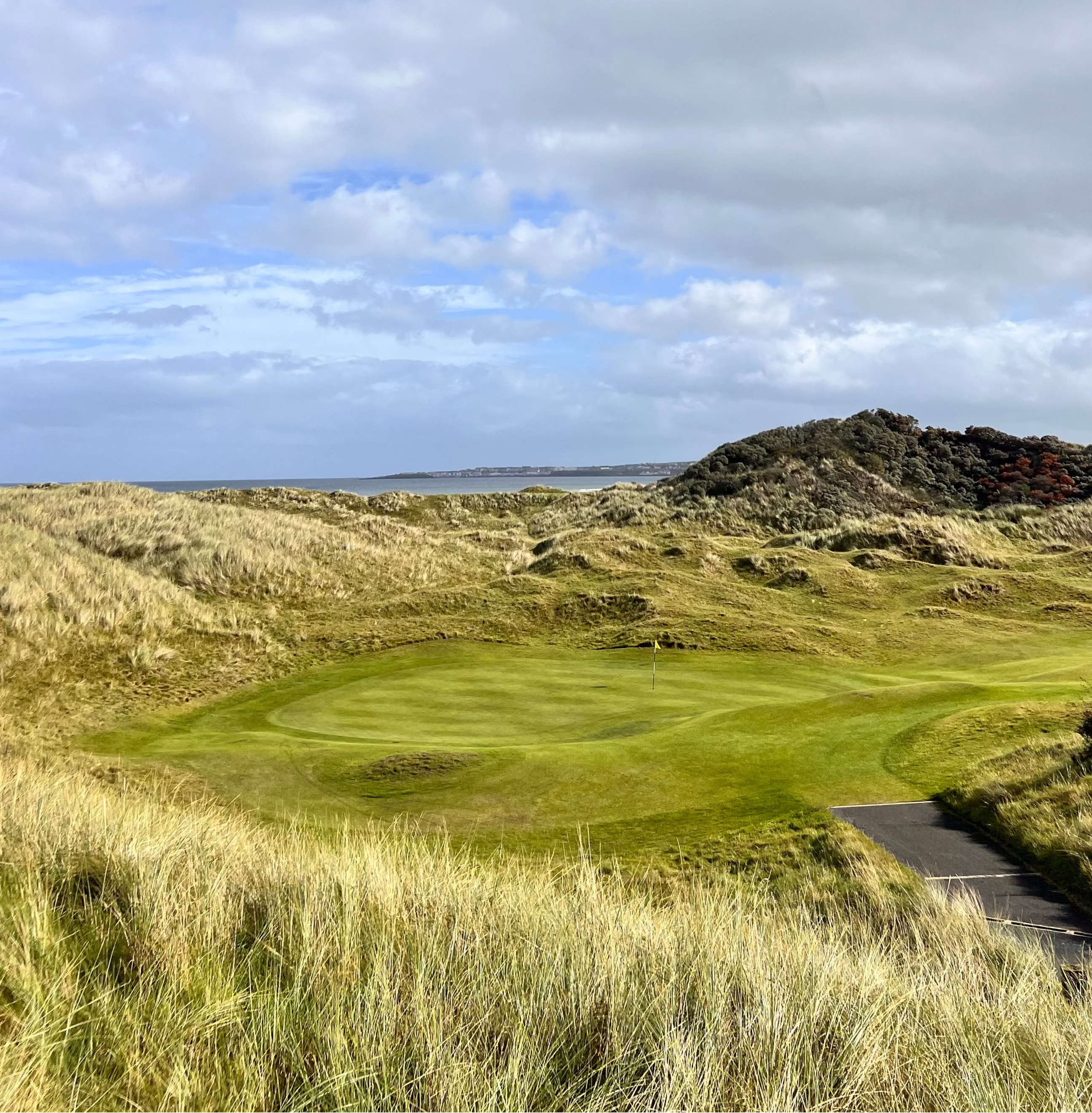 A green at Castle Rock golf course with green grass and sand dunes under a cloudy sky